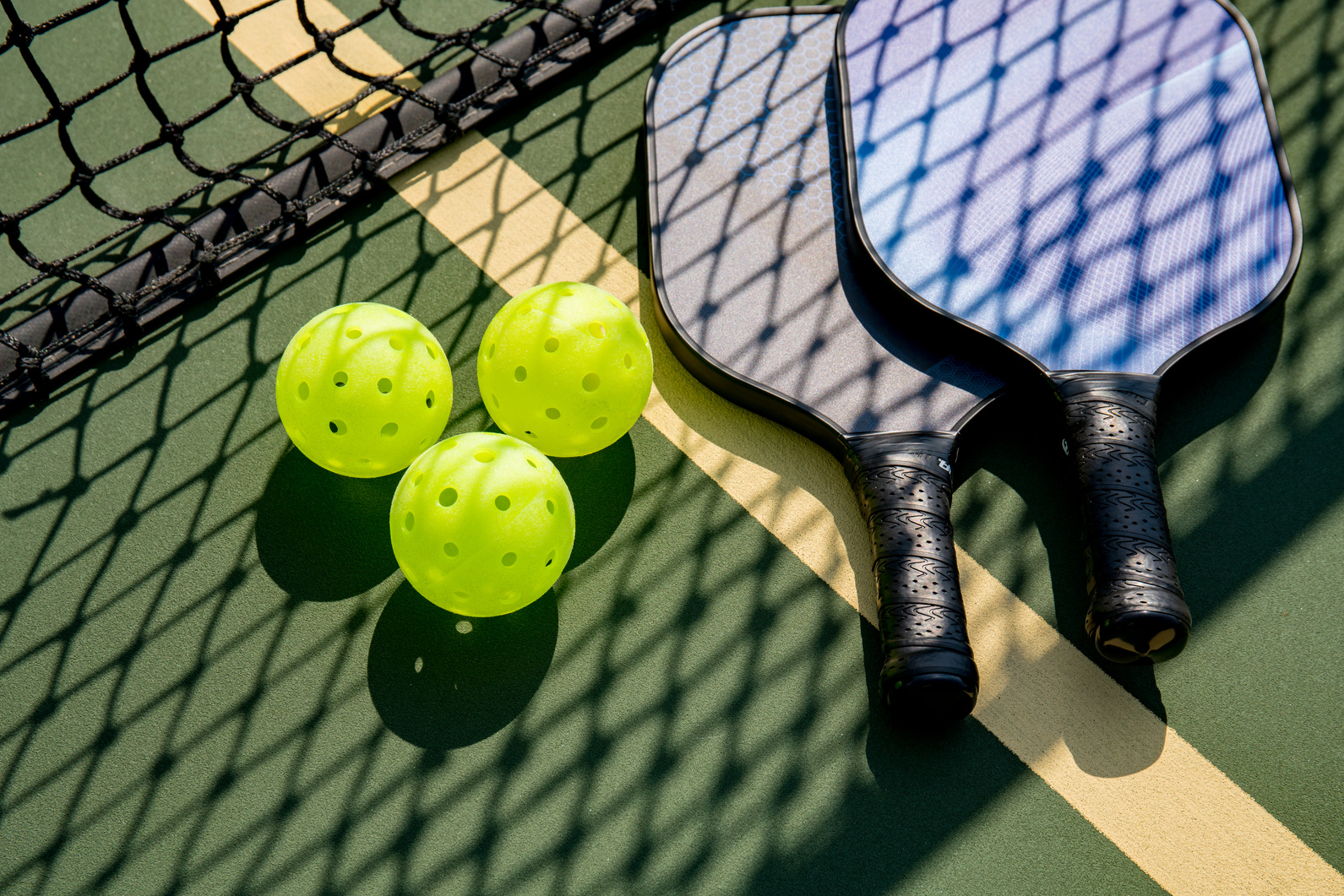 Pickleball paddles and ball in shadow of net
